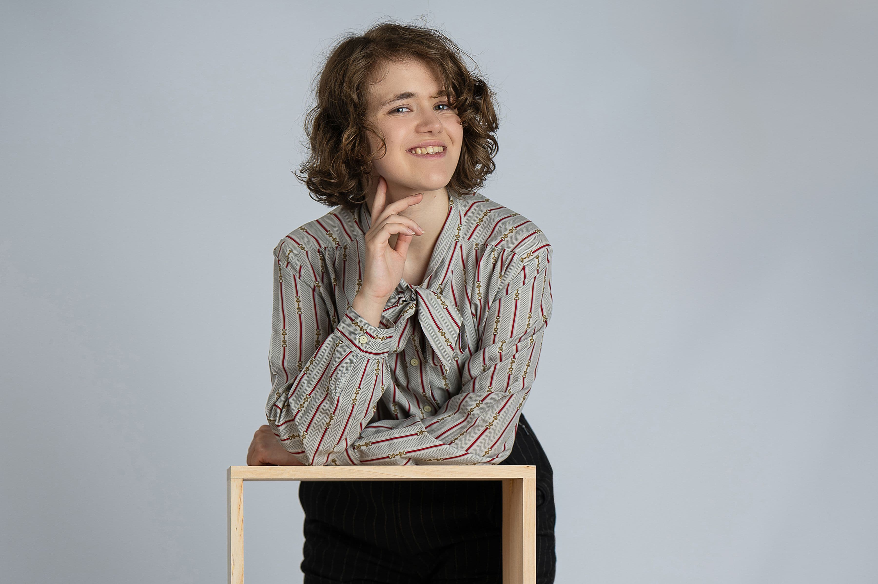 Młodzieżowa sesja fashion w szkole — uczennica w koszuli w paski oparta na drewnianym kubiku na jasnym tle studyjnym